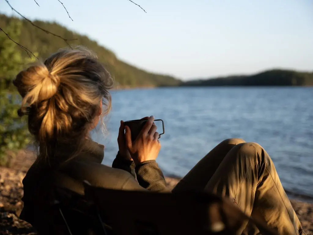 Frau trinkt bei Sonnenuntergang Kaffee am See