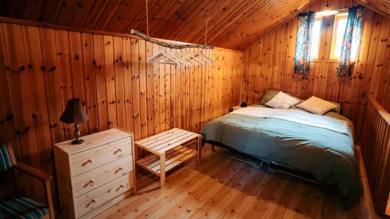 Gemütliches Schlafzimmer in einer Holzhütte mit Bett, Kommode und Kleiderbügeln