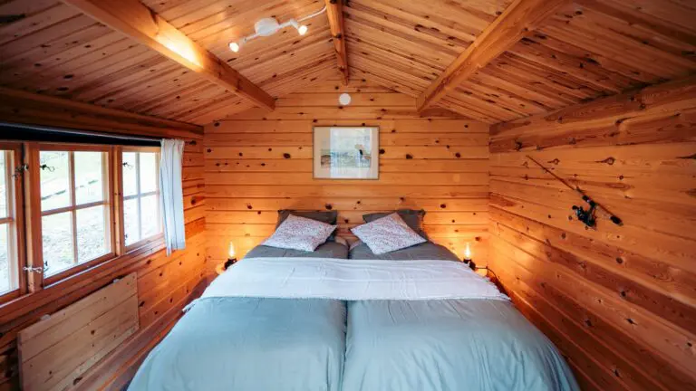 gemütlicher Innenraum einer Holzhütte mit zwei Einzelbetten und Angelrute