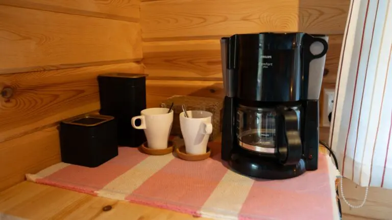 Kaffeemaschine und Tassen auf einer gestreiften Matte in einer Holzhütte