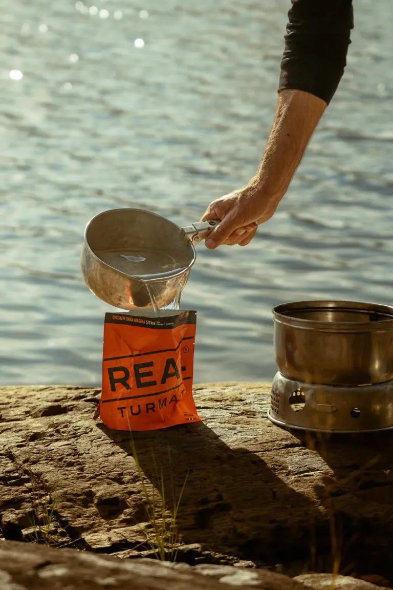 Person, die an einem See Wasser in einen Beutel mit Fertigmahlzeit gießt
