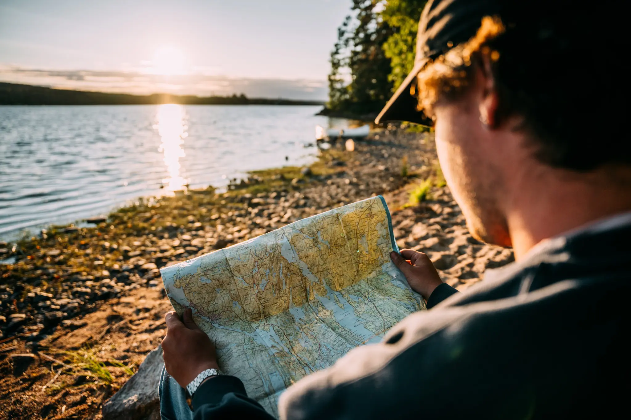 Person mit Kappe liest bei Sonnenuntergang am See eine Karte