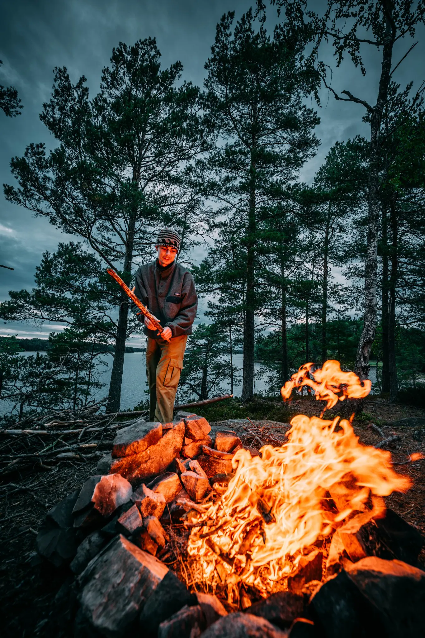 person tending a campfire by a lake in a forest