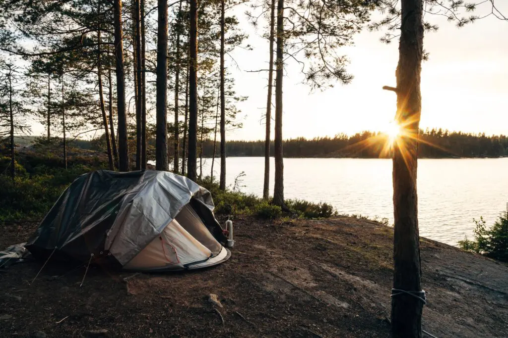 tent by a lake in a forest at sunset