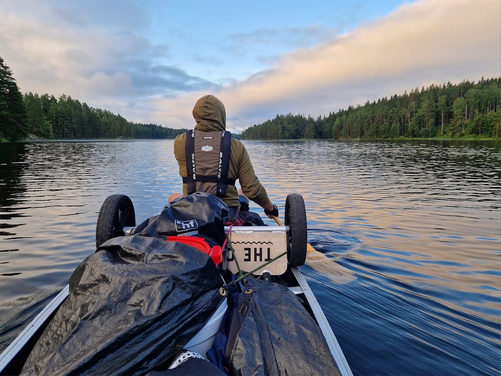 Voyageur entrain de pagayer avec ses affaires dans son canöe recouvertes d'une bâche étanche.