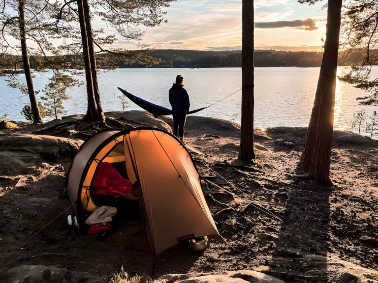 Ein beleuchtetes Kuppelzelt auf einem felsigen Wildcampingplatz an einem großen See in Schweden bei stimmungsvoller Abenddämmerung.